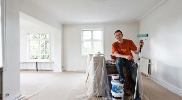 Målare med roller redo att måla bakom elementet i ett rum under renovering.