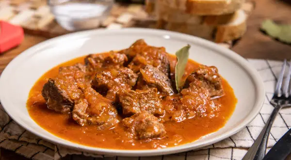 Sabrosa carne guisada con tomate, tiernos trozos de carne en una rica salsa, servida en un plato blanco.