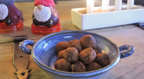 En blå skål med chokladpraliner, perfekta som julgodis utan socker. I bakgrunden syns tomteljus och adventsljusstake.