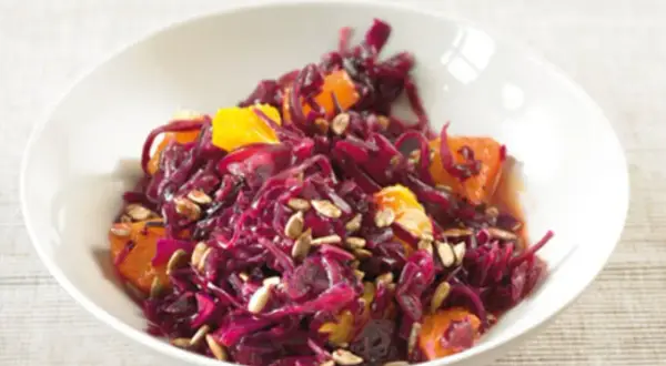 Rotkohlsalat mit Apfel und Orange, garniert mit Sonnenblumenkernen, in einer weißen Schüssel.