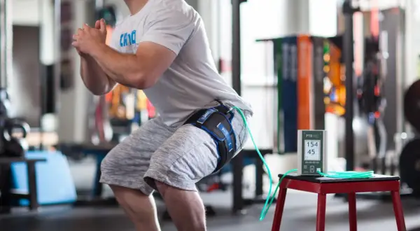 Un athlète en plein squat, équipé d'un appareil de bfr kiné à la cuisse, mesure ses performances.