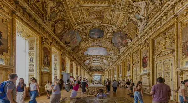 Prunkvolle Deckenmalereien und goldene Verzierungen im Louvre von innen. Besucher bestaunen die Kunstwerke in der langen Galerie.