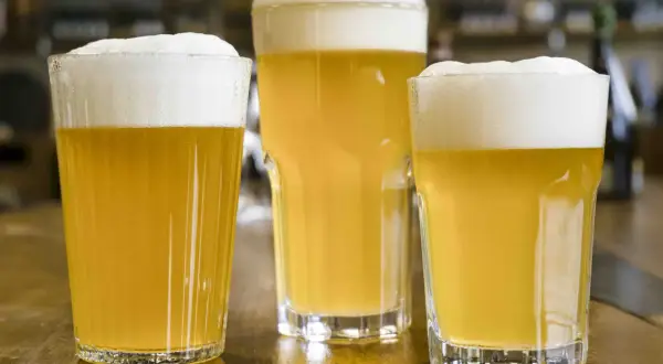 Tre bicchieri di birra dorata con schiuma bianca, pronti per essere gustati. Gli ingredienti della birra, acqua, malto e luppolo, si trasformano in questa bevanda rinfrescante.
