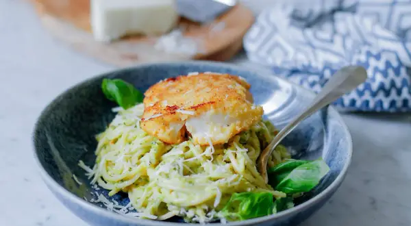 Pyszny makaron z rybą w panierce, posypany parmezanem i udekorowany bazylią. Danie wygląda apetycznie i zachęca do spróbowania.