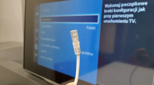 Kabel sieciowy Ethernet zbliżenie na wtyczkę RJ45 na tle ekranu telewizora z menu ustawień.