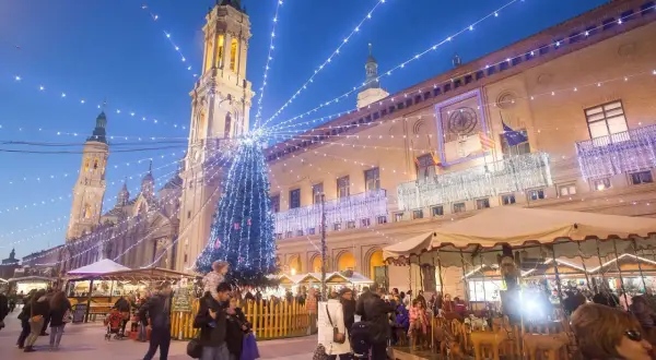 Mercado navideño en Zaragoza con árbol iluminado y gente paseando. Descubre qué ver en Zaragoza en Navidad.