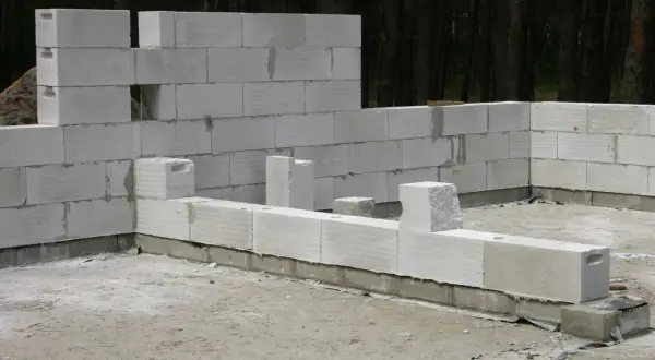 Budowa domu z betonu komórkowego. Ściany wznoszone z białych bloczków, w tle las.