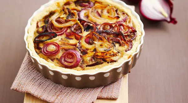 Tarte à l'oignon dorée et appétissante, garnie d'oignons caramélisés et d'une pâte croustillante. Un délice visuel et gustatif.