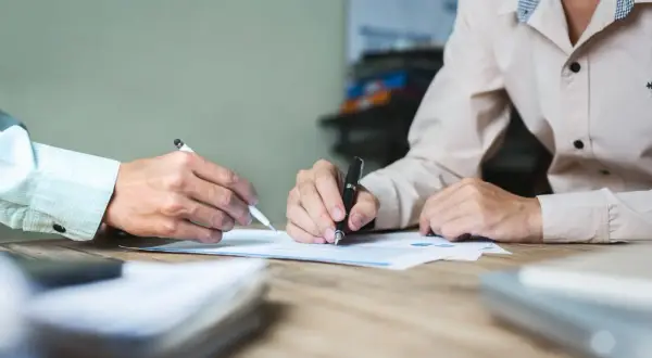 Dwie osoby przy biurku analizują dokumenty. Jedna z nich pisze, druga wskazuje coś na papierze. Może to być pomoc w procesie jak odzyskać pieniądze z obligacji Getin Noble Bank.
