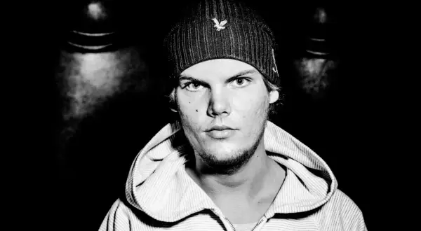Czarno-białe zdjęcie Avicii w czapce i bluzie z kapturem, patrzącego prosto w obiektyw.