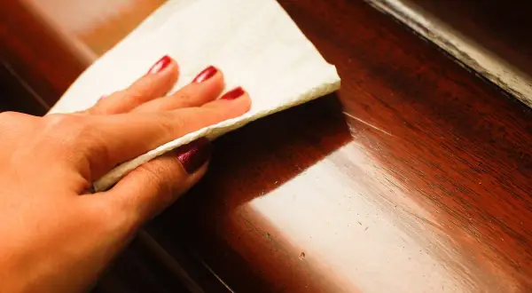 Main d'une femme avec vernis bordeaux, essuyant une table en bois verni pour savoir comment enlever une rayure.