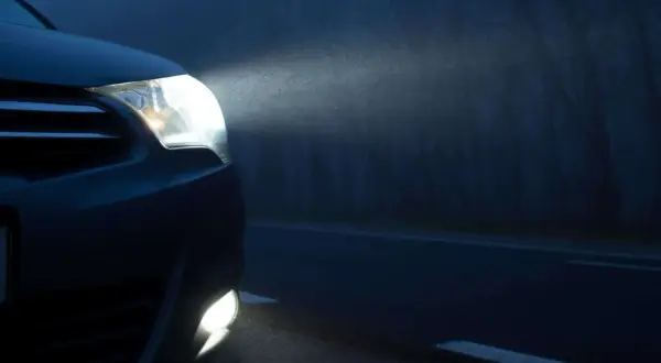 Las luces de posición de un coche iluminan la niebla en una carretera oscura, revelando el camino y los árboles a los lados.