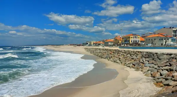 Sonne, Sand und Wellen an der Costa Verde, Portugal. Häuser mit roten Dächern säumen den Strand, geschützt von einer Steinmauer.