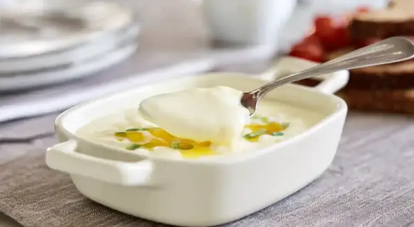 En sked lyfter krämig bechamelsås ur en vit skål, perfekt för ditt bechamelsås recept.