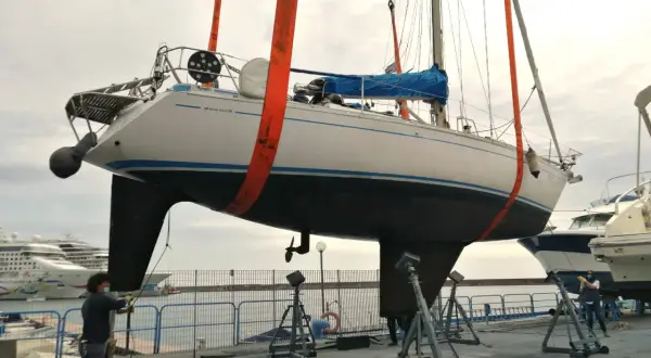 Barca a vela sollevata da gru, pronta per la manutenzione dello scafo e l'applicazione dell'antivegetativo.
