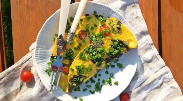 Pyszny omlet ze szpinakiem i pomidorkami, posypany szczypiorkiem, czeka na talerzu. Idealny na letnie śniadanie.