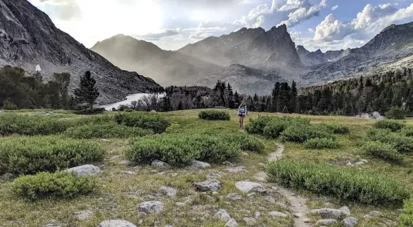 Wanderer auf dem Continental Divide Trail wandern durch eine bergige Landschaft mit einem See und bewaldeten Hängen.