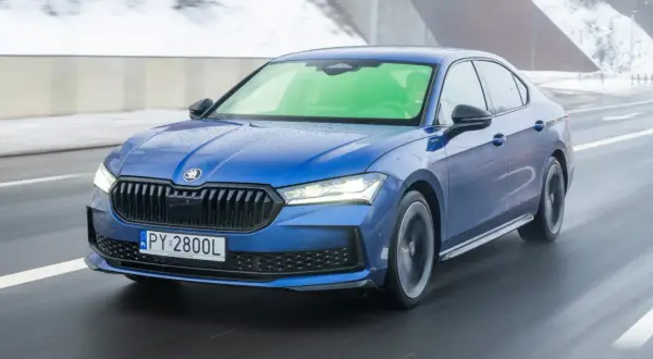 Niebieska Skoda Superb 2.0 TSI pędzi po mokrej drodze, tworząc wrażenie prędkości.
