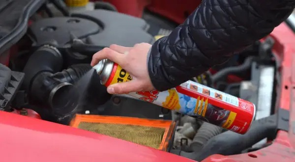 Ręka trzyma puszkę z preparatem do rozruchu silnika, rozpylając go w okolicy filtra powietrza. Czy odpalanie na plaka jest szkodliwe?