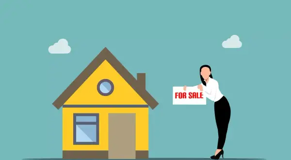 Kobieta z tabliczką "FOR SALE" przy żółtym domku. Zastanawiasz się, kiedy możesz sprzedać mieszkanie bez podatku?