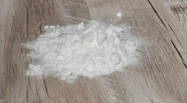 Ein Haufen weißes Pulver, wahrscheinlich Natriumascorbylphosphat, liegt auf einer Holzoberfläche.