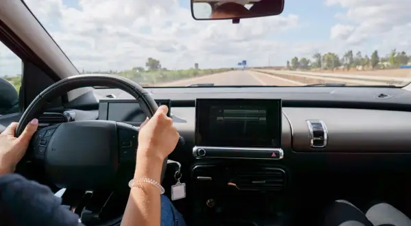 Vue du **rétro intérieur position nuit** d'une voiture. Mains sur le volant, route dégagée sous un ciel nuageux.