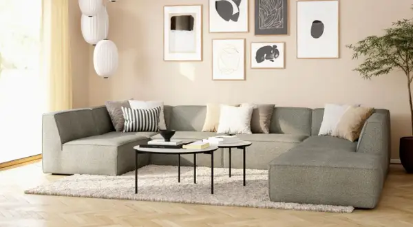 Gemütliches Wohnzimmer mit beiger Wand, einem großen grauen Sofa, Kissen und Kunstwerken.