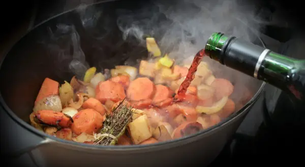 Verduras cocinándose en una olla, se vierte vino tinto. El vapor sube, indicando que el alcohol se evapora rápido.