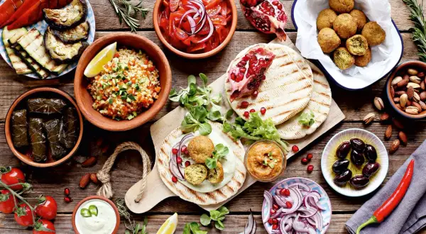 Vielfalt an arabischem Essen: Falafel, gefüllte Weinblätter, Bulgursalat, gegrilltes Gemüse, Hummus, Oliven und Granatapfel.