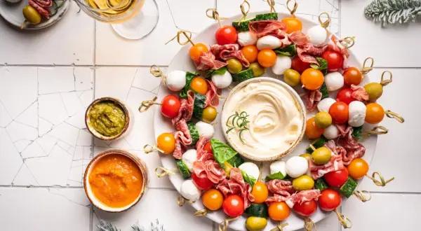 Kolorowe przystawki na zimno w kształcie wieńca, z mozzarellą, pomidorkami, oliwkami i salami, podane z dipami.