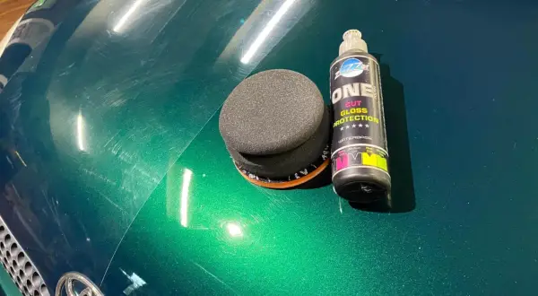 Zestaw do polerowania auta: gąbka i butelka z preparatem "ONE CUT GLOSS PROTECTION". Widać zarysowania na zielonym lakierze, które można usunąć.