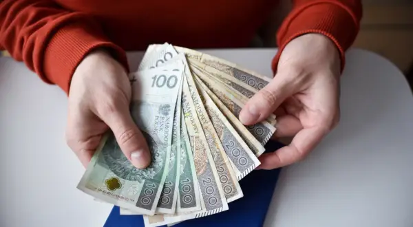 Dłonie trzymają plik polskich banknotów. Zastanawiasz się, ile wynosi składka zdrowotna dla emeryta?