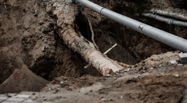 Gros plan sur un ancien tuyau en plomb dans une tranchée, à côté d'un nouveau tuyau gris. Travaux de rénovation dans une maison.