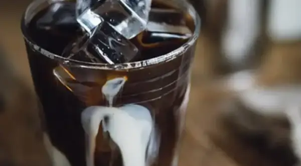 Ett glas iskaffe på snabbkaffe med mjölk som rinner ner längs glaset och isbitar som flyter i kaffet.