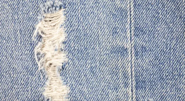 Zbliżenie na niebieski denim z widocznym przetarciem. Dowiedz się, jak zrobic przetarcia na dzinsach, by nadać im stylowy, znoszony wygląd.