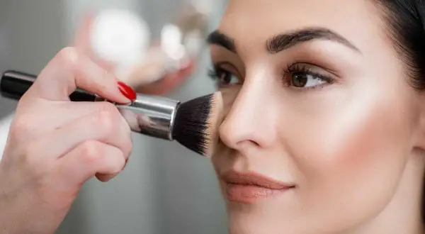 Mano con pennello applica terra sul viso per un look naturale.