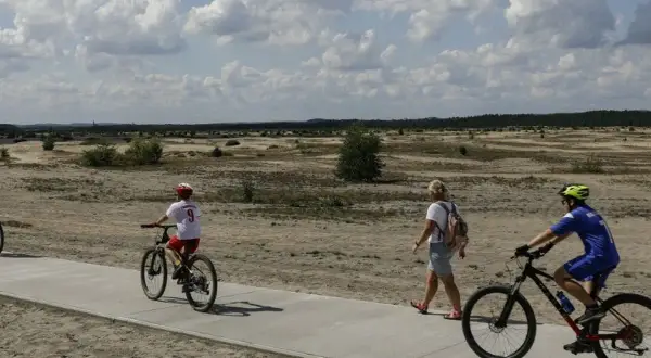 Ludzie na rowerach i pieszo na ścieżce rowerowej w krajobrazie pustynnym.