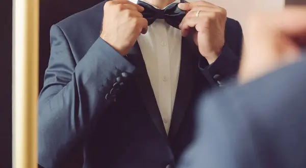 Mann im dunklen Anzug richtet Fliege, bereit für die Hochzeit. Was kostet ein Hochzeitsanzug?