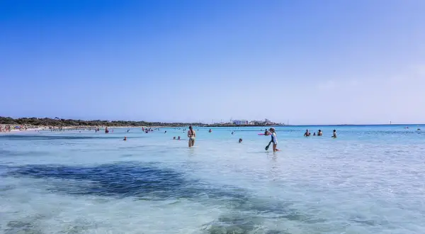 Słoneczny dzień na plaży Es Trenc. Ludzie kąpią się w krystalicznie czystej wodzie, ciesząc się wakacjami.