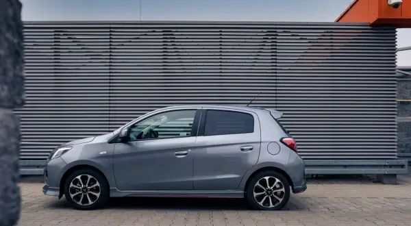 Szary Mitsubishi Space Star stoi na tle nowoczesnej, szarej ściany z poziomymi żaluzjami.