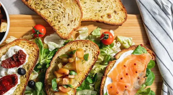 Bruschette senza pomodoro: fette di pane tostato con salmone, crema, pomodori secchi e verdure fresche.