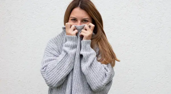 Frau versteckt sich hinter ihrem kuscheligen Pullover, der sich statisch aufgeladen anfühlt.