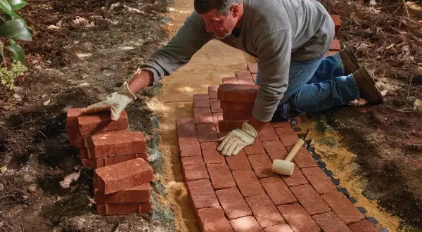 Man laying red bricks to create a new brick walkway in a garden.