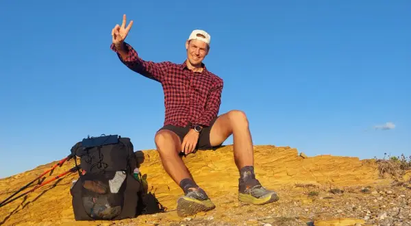 Glücklicher Wanderer mit Rucksack und Stöcken auf einer felsigen Anhöhe, genießt die Aussicht nach einer Etappe des Fischerpfads in Portugal.