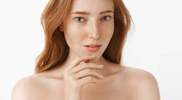 Ruda dziewczyna z piegami, których urok podkreśla naturalna melanina. Jej spojrzenie przyciąga uwagę.