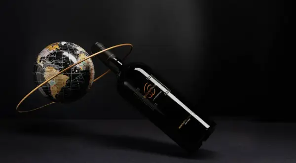 Elegancka butelka Sessantanni Primitivo di Manduria, otoczona złotym pierścieniem, obok globusa.