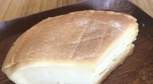 Un morceau de fromage à pâte molle, à la croûte orangée et à l'odeur prononcée, servi sur un plateau en bois.