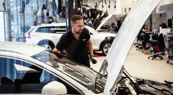 Mekaniker inspekterar en bil med öppen motorhuv. Frågan "hur ofta ska man serva bilen" är relevant för att hålla fordonet i toppskick.