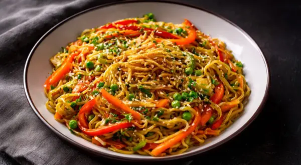 Schüssel mit chinesischen Bratnudeln, garniert mit Erbsen, Paprika und Sesam.