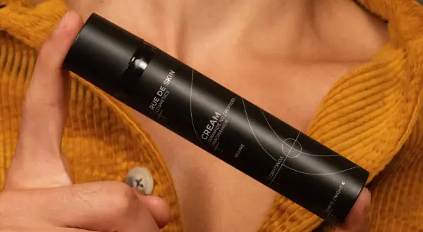 Dłoń trzyma czarny flakon kremu z napisem "Niacynamid". Czy wybrać retinol czy niacynamid?